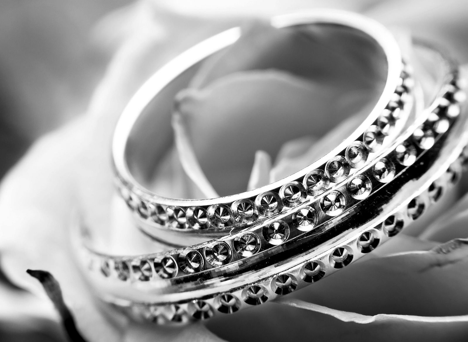 Two silver rings with embedded stones resting on a blurred floral background, in black and white.
