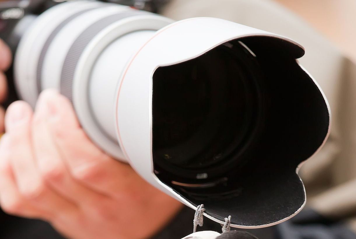 A photographer holding a professional camera with a large zoom lens.