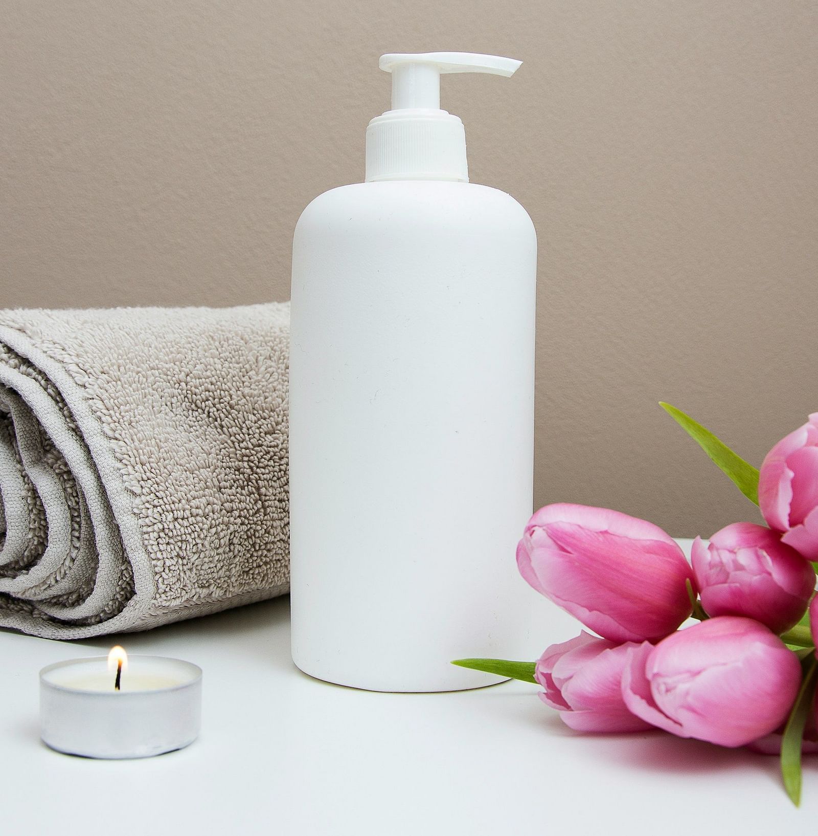 a lotion bottle placed in between of tulips and a towel at a spa