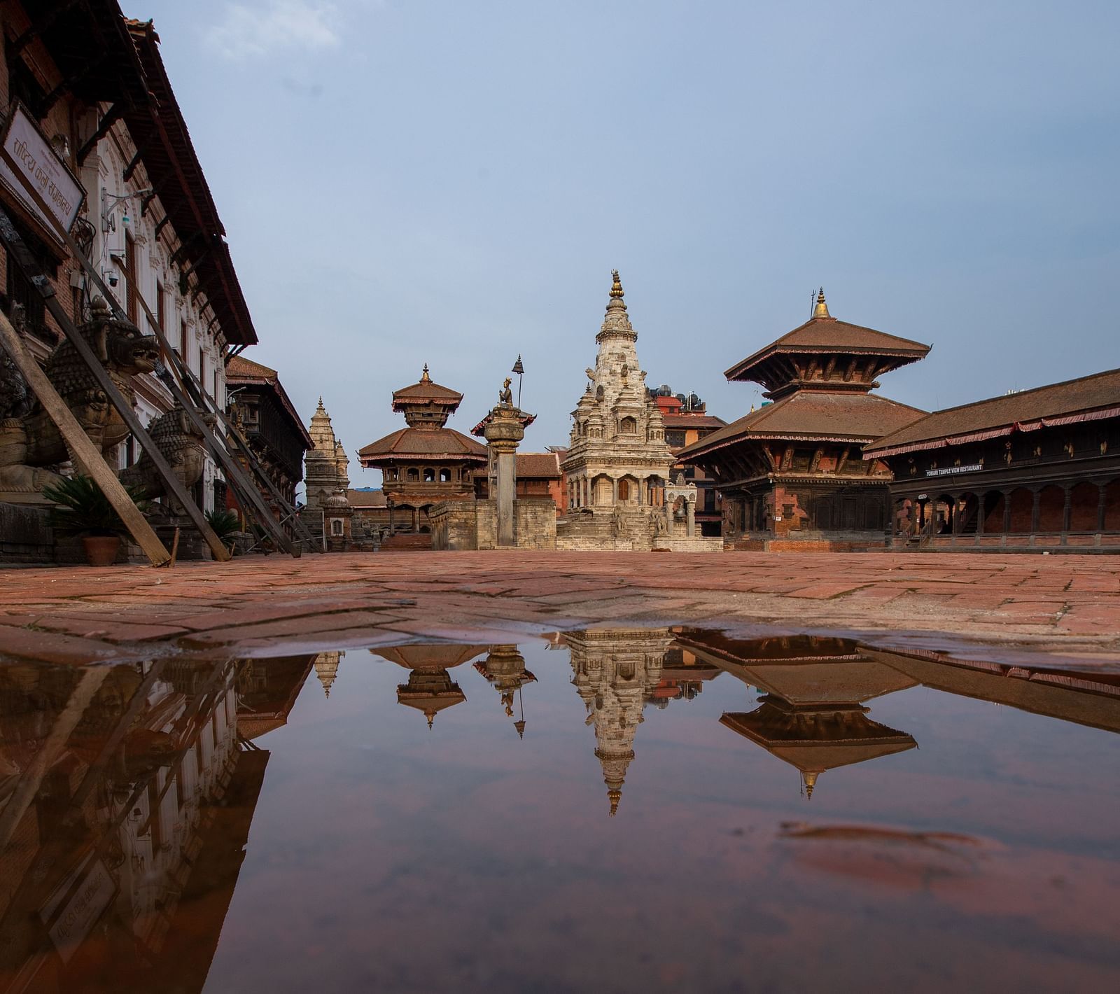 A facade view of the bhaktapur durbar square where a puddle of water is reflecting the structure