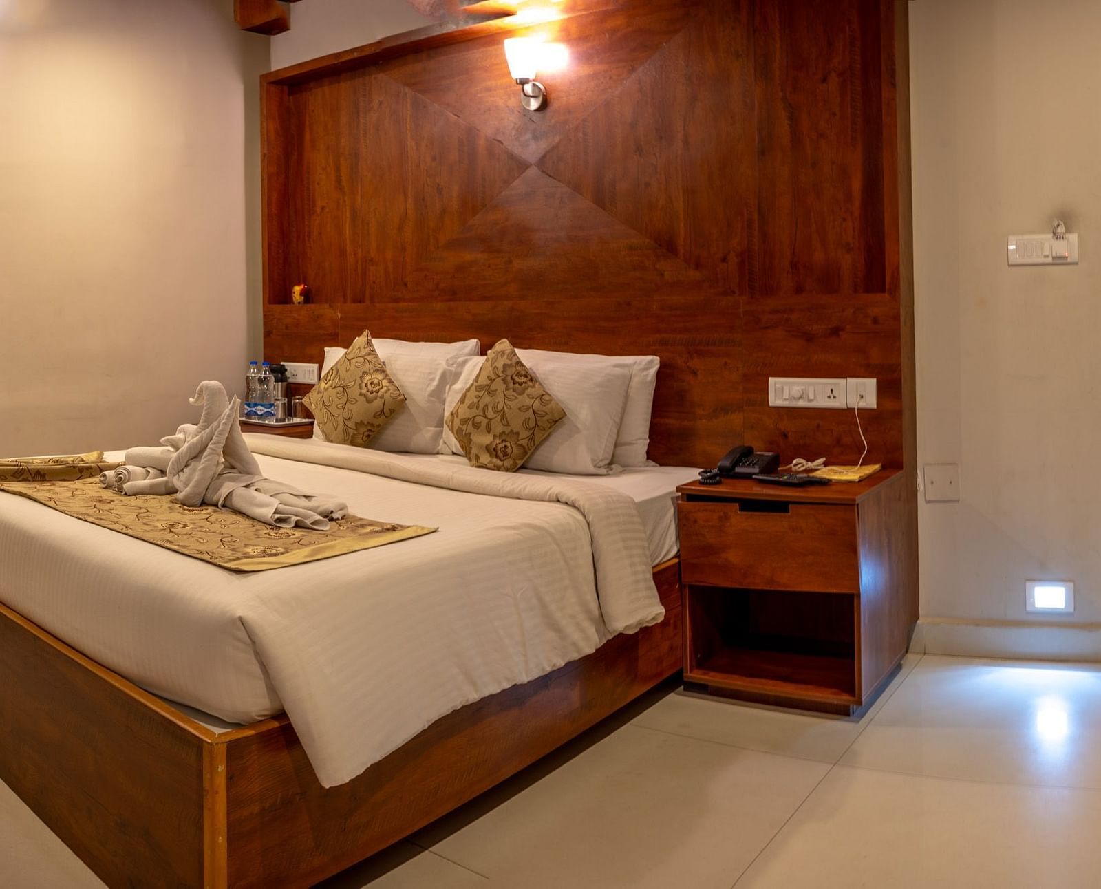 Superior Room featuring a king size bed with a wooden frame and bedside table, illuminated by warm lighting | Woodstock Resorts, Coorg