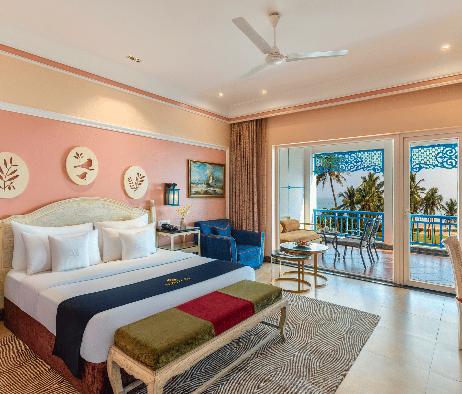 Deluxe room with a king bed, a bench, an armchair and a balcony overlooking the sea and palm trees at MAYFAIR Palm Beach Resort, Gopalpur-on-Sea.