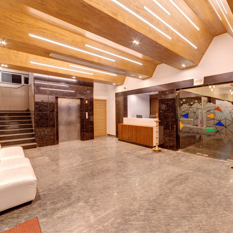 A white sofa, grey marble floor, wooden ceiling, and stairs in the lobby of Icon Express By Bhagini, Mahadevapura.