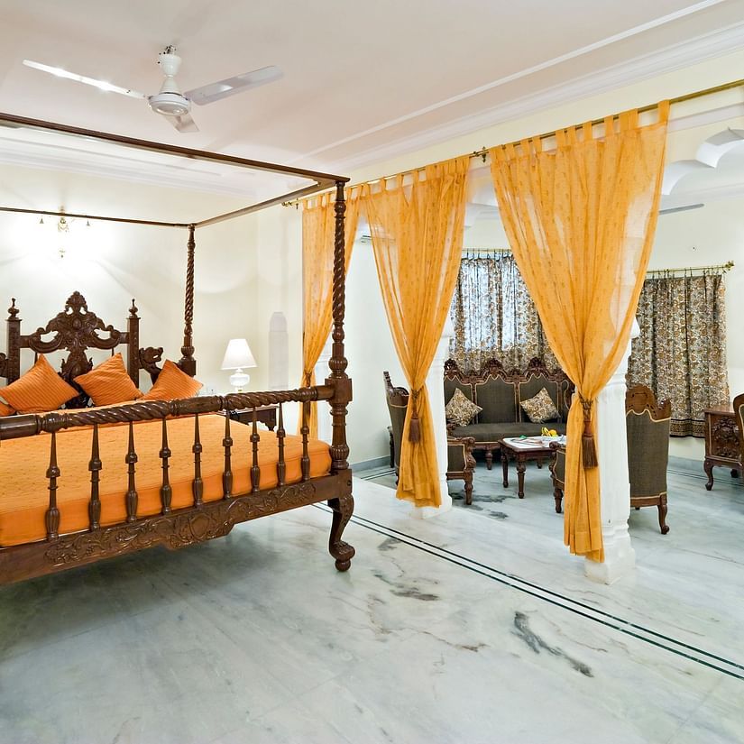 A king bed with lamps on the side tables and sofas in the living room inside the suite - Mandawa Haveli, Jaipur