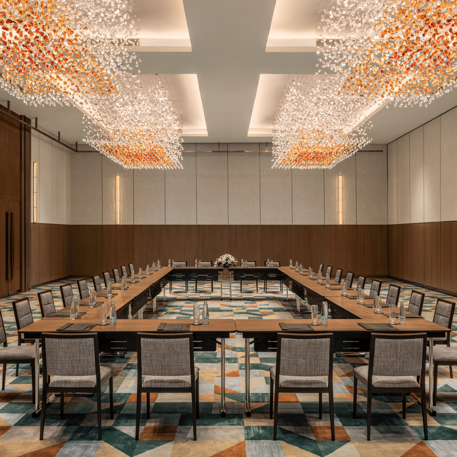 The large meeting room of Ballroom 3 configured in board room arrangement with warm crystal chandeliers and colourful patterned carpet at The Residency Towers Chennai.