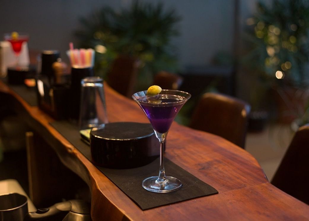 A purple coloured cocktail poured in a martini glass placed on a counter.