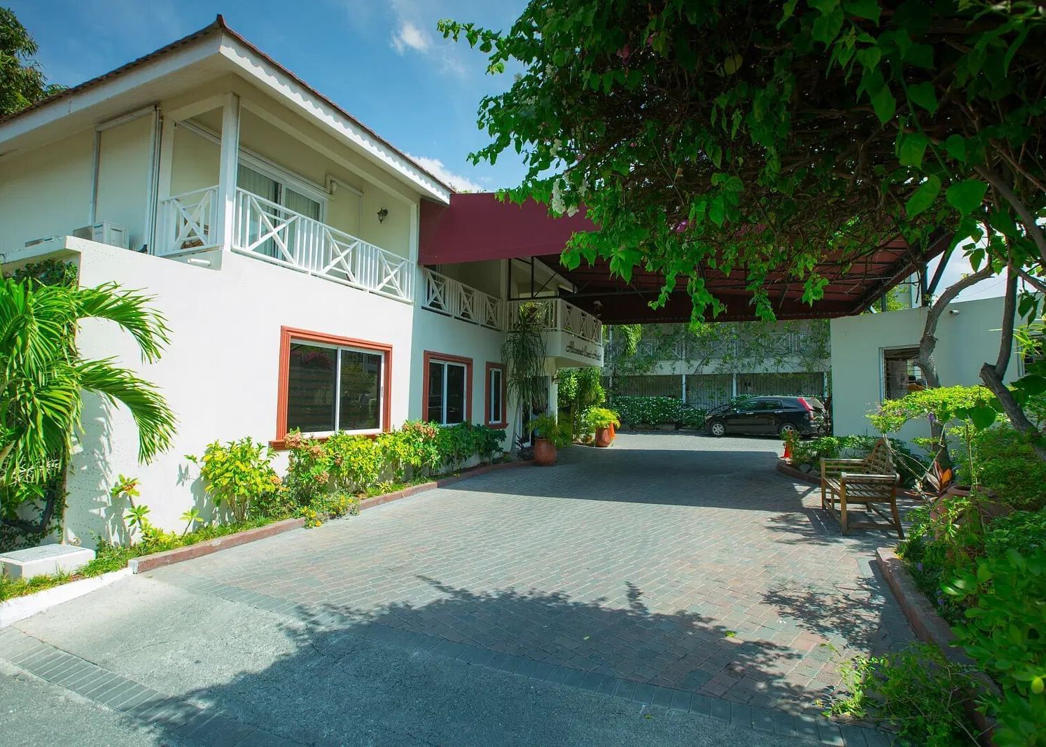 A white house with a roof is seen from a paved driveway leading up to its entrance | Altamont Court, Jamaica