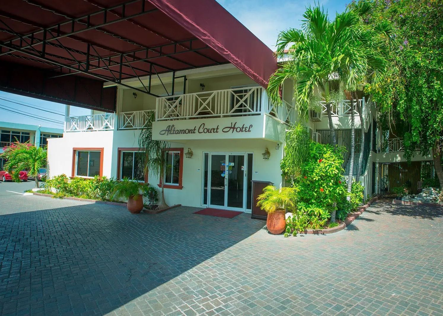 A low-angle shot of a white building with a covered entrance and lush green foliage | Altamont Court, Jamaica