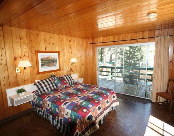 A warm, wood-paneled cabin interior revealing a bedroom with a patterned bedspread and an open doorway to another room | Snow shoe