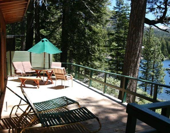 A wooden deck with an outdoor dining area and lounge chairs overlooks a river and lush green trees | Wolf