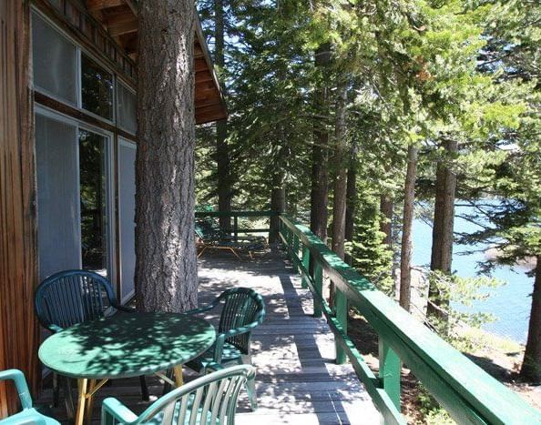 A cabin with a large deck overlooks a serene lake, surrounded by towering pine trees | Black Bear