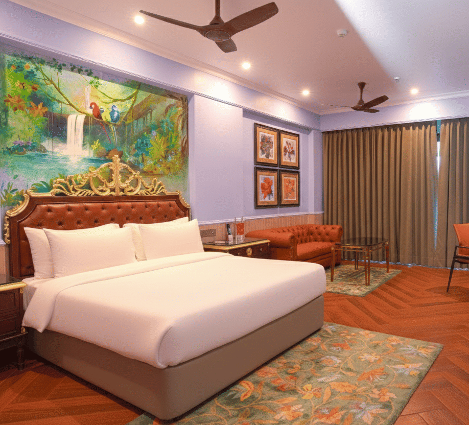 A well-lit room featuring a plush double bed, artistic headboard, wall paintings, writing desk, wooden flooring and ceiling fan with floor-to-ceiling curtains at MAYFAIR Bay Resort, Paradeep.