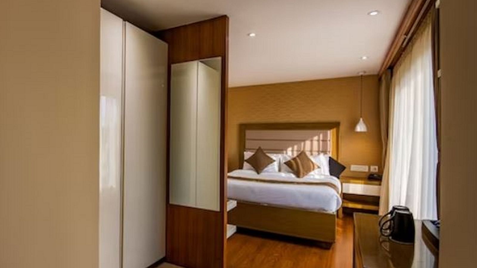 A view into a standard hotel room featuring a plush bed, tasteful decor, and warm lighting, seen through an open doorway at Yashshree The Imperial Inn, Siliguri.