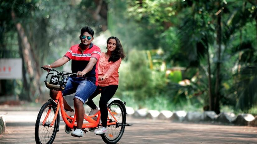 A couple riding a tandem bicycle on a tree-lined path - Black Thunder, Coimbatore