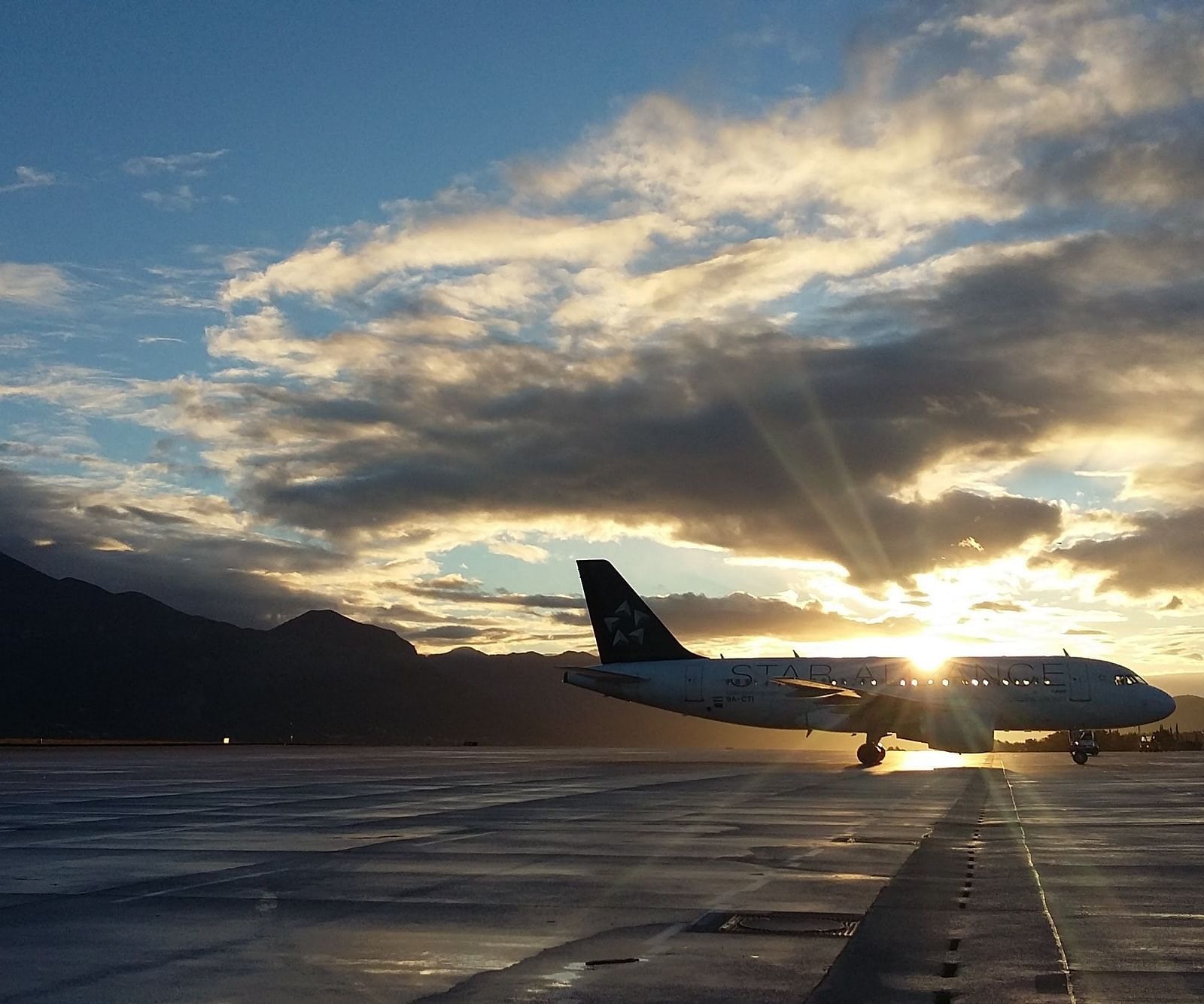 an aeroplane parked in a runway with the sun setting in the background