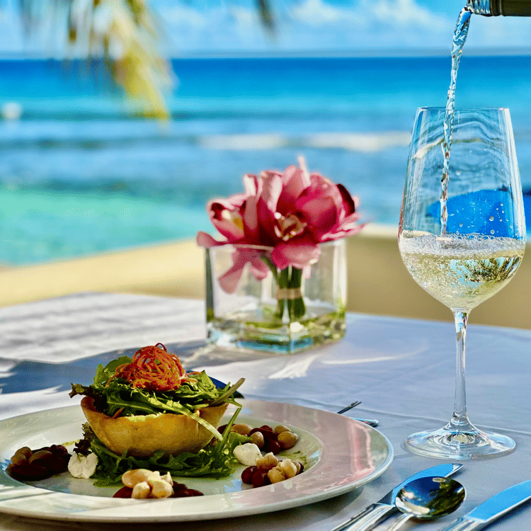 Close-up of an elegantly plated vegetarian meal with wine being poured into a glass on an outdoor table overlooking the ocean at The Soco Hotel.