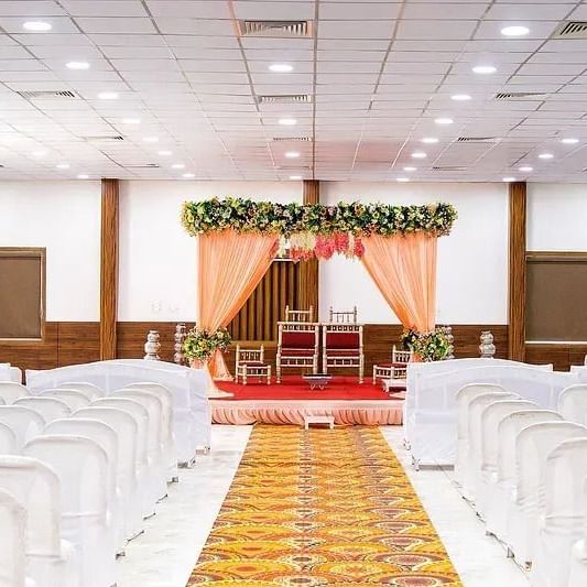 An indoor banquet hall with white chairs arranged for a ceremony at Daksh Resort and Amusement Park.