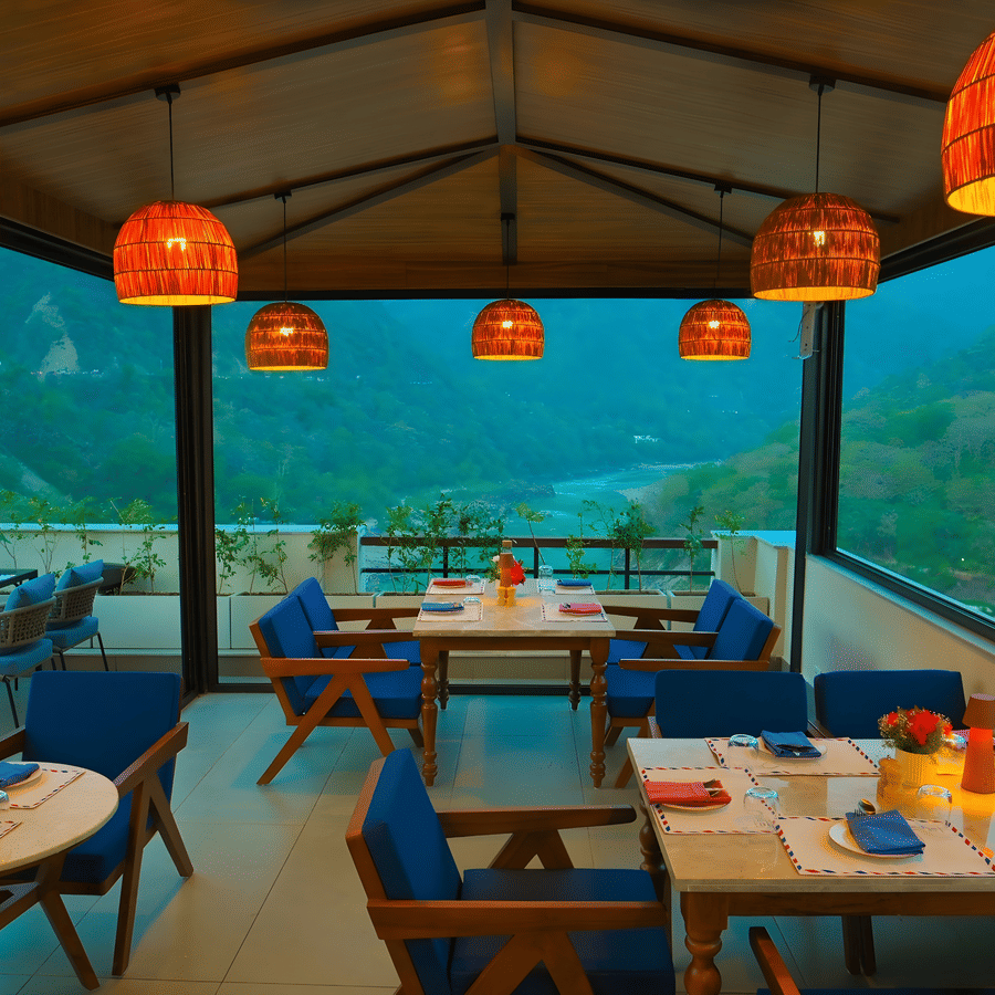Window side dining area at The Terrace, Aloha on the Ganges, Rishikesh, overlooking the surrounding mountains through floor to ceiling glass panels.