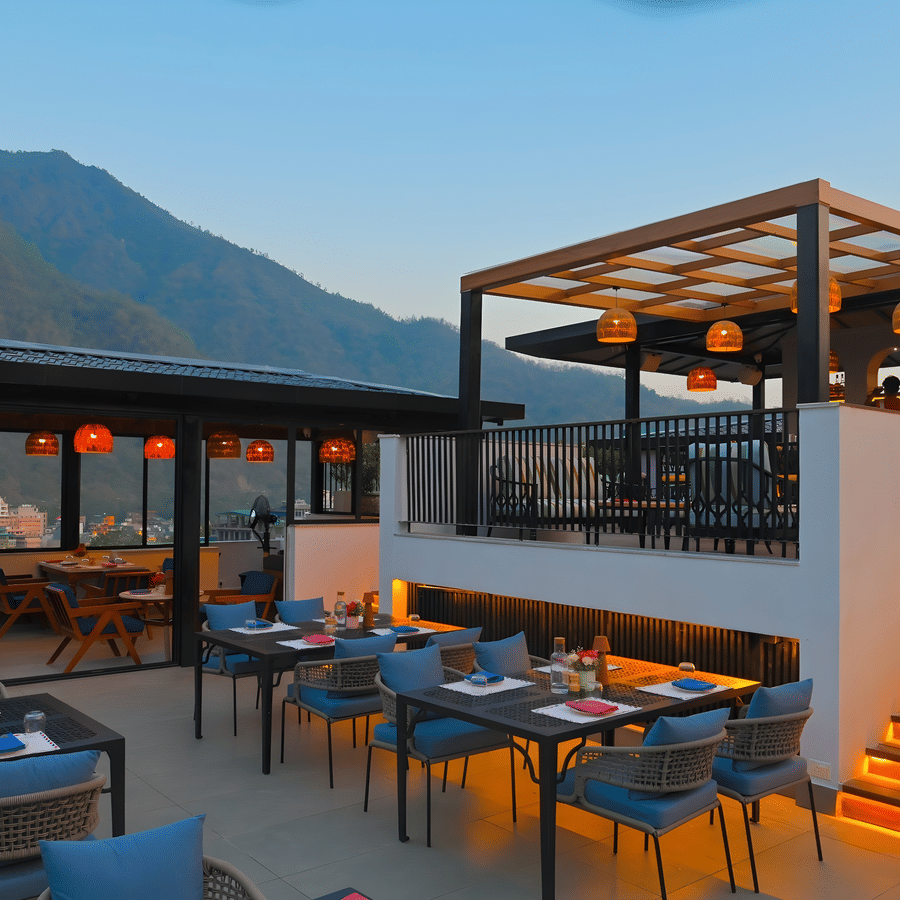 Rooftop dining area at The Terrace, Aloha on the Ganges, Rishikesh, featuring outdoor seating, illuminated staircase, and mountain views at dusk.