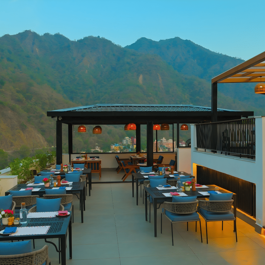 Spacious rooftop restaurant at The Terrace, Aloha on the Ganges, Rishikesh, featuring outdoor tables, ambient lighting, and panoramic mountain views.