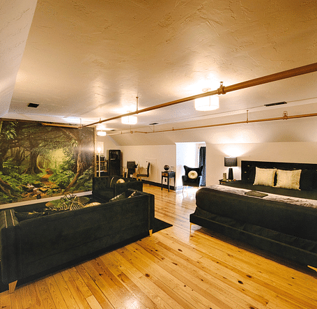 a spacious bedroom with a cozy double bed and black couch set in the common seating area with a jungle mastiff made in the feature wall of the suite - Historic Tapoco Lodge