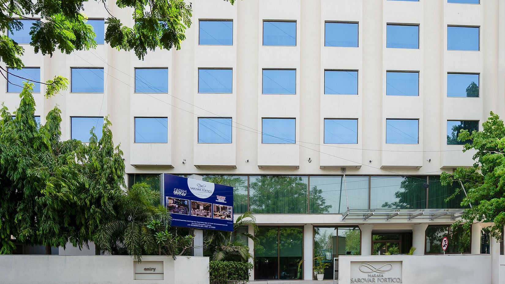  A facade image of the Marasa Sarovar Portico, Rajkot with trees around.