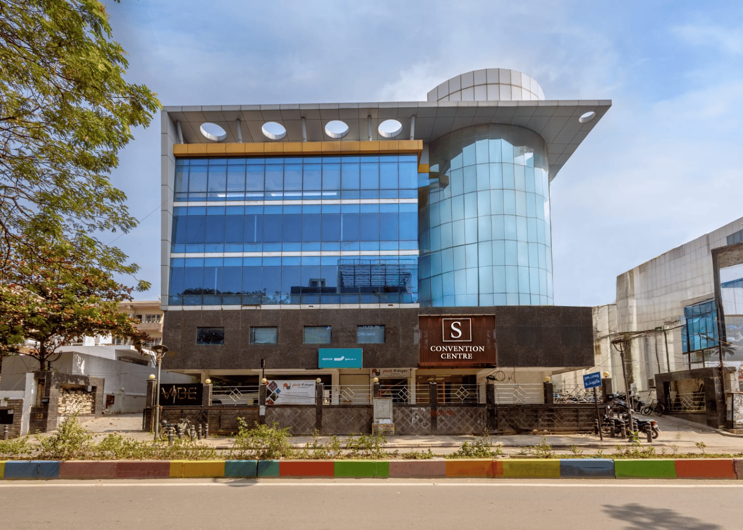 The modern glass exterior of the S Convention Centre of S Hotels, Chennai, showcasing its multi-story architecture and prominent signage.