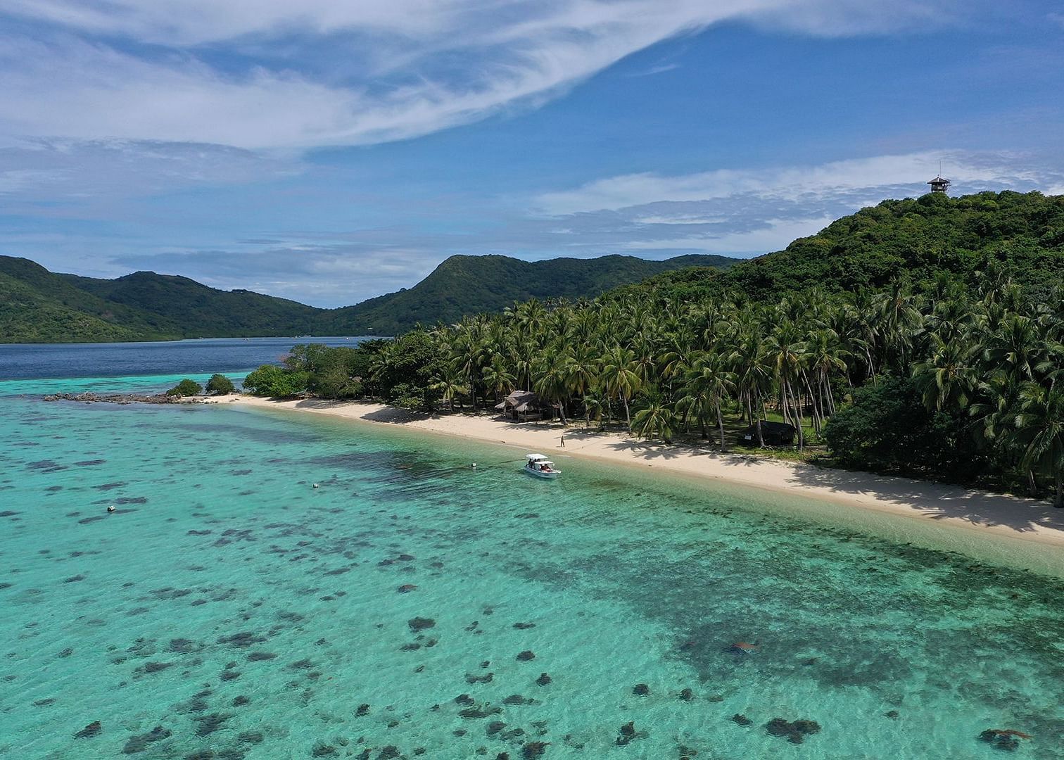Aerial view of a beach and turquoise water near the forested coastline of Flower Island Resort.