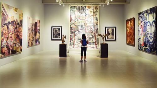 A girl staring at paintings hung on the wall in a museum