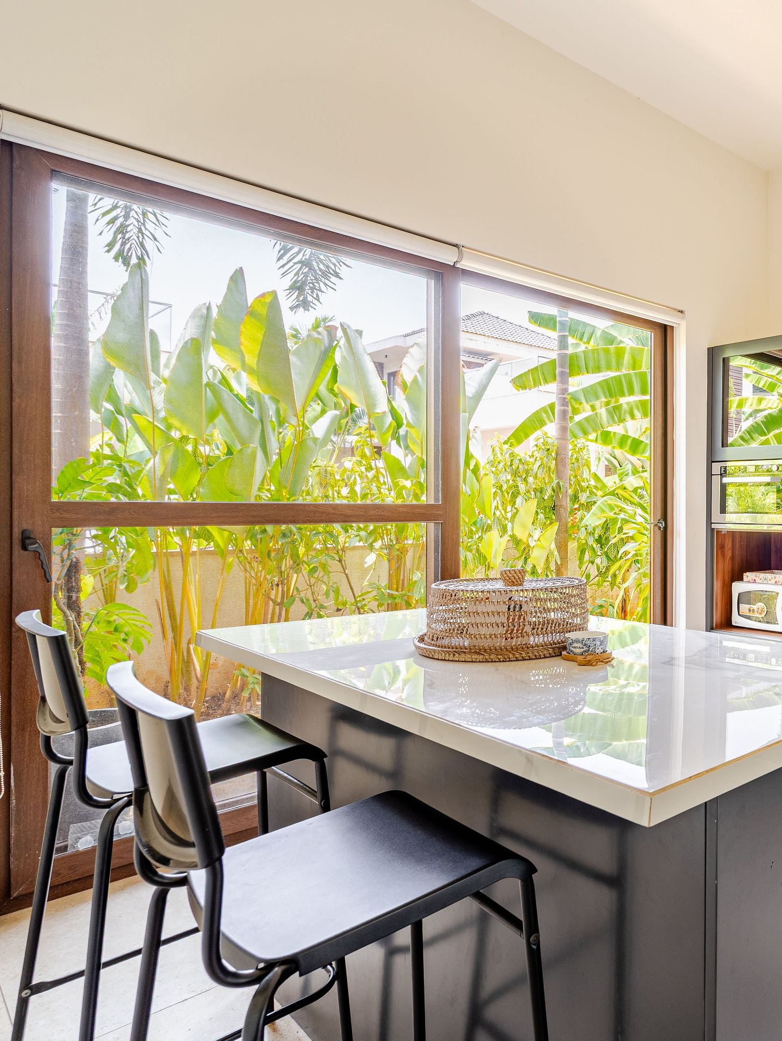 Modern kitchen at Lindsay Manor with a centre island, bar stools, cabinets, microwave, and large windows overlooking greenery.