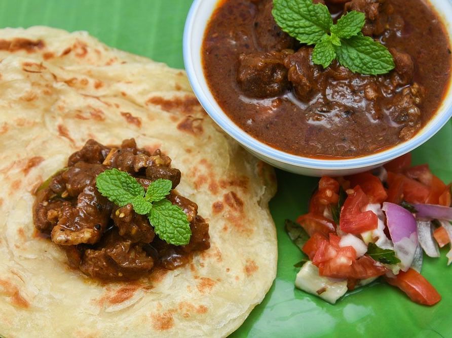 Plate of Kerala parotta served with spicy mutton curry and fresh salad garnishes.