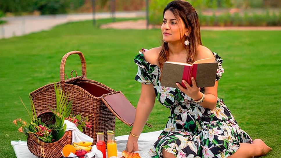 A girl reading a book in a picnic setup on the lawn, with details of the summer package inclusions displayed