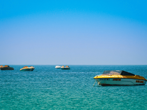 Numerous boats on the Arabian Sea next to Colva Beach with blue-green waterbody and blue sky seen.