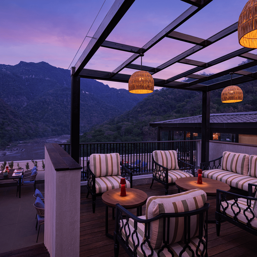 Open air lounge at The Terrace, Aloha on the Ganges, Rishikesh, featuring cushioned seating beneath a pergola with mountain views at twilight.
