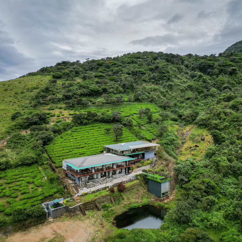 An aerial shot of the the resort surrounded by greenery and mountains on all sides and clear sky in the background | Ibex Stays and Trails