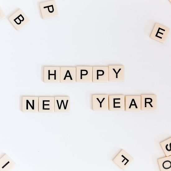 happy new year written from scrabble tiles with other scrabble tiles on the side