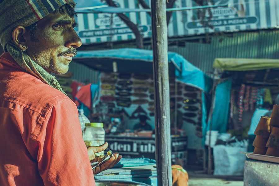 alt-text An indian street food vendor in a red shirt, looking towards the sun's direction while keeping his vision in shade.