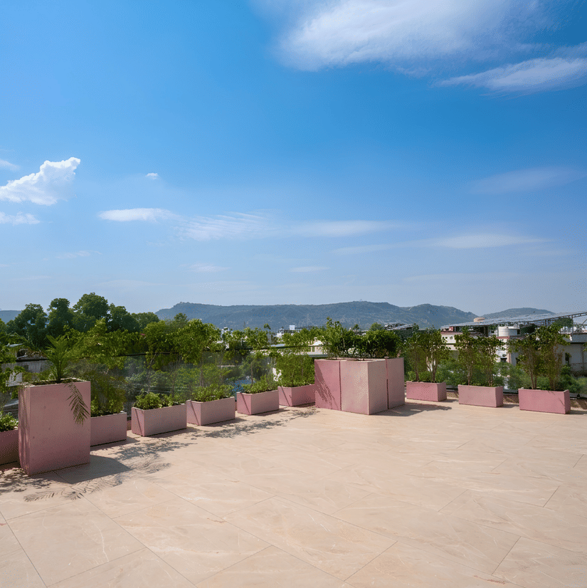 An outdoor terrace area with planters along the edge, overlooking trees and distant hills under a sky with clouds.