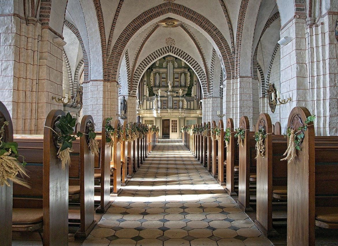 A stunning view of the interior of a church, with neatly arranged wooden pews, high arches, and decorative floral arrangements.