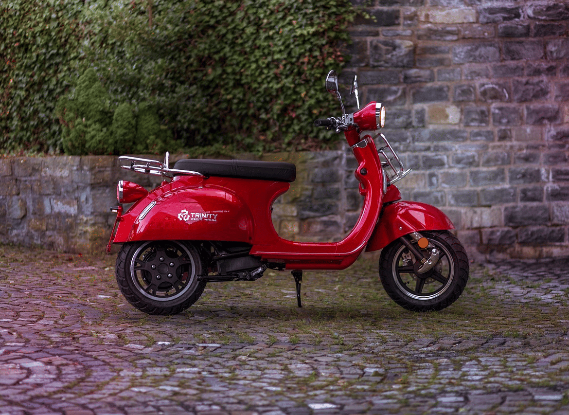 A red scooter parked on a cobblestone ground next to a stone or brick wall