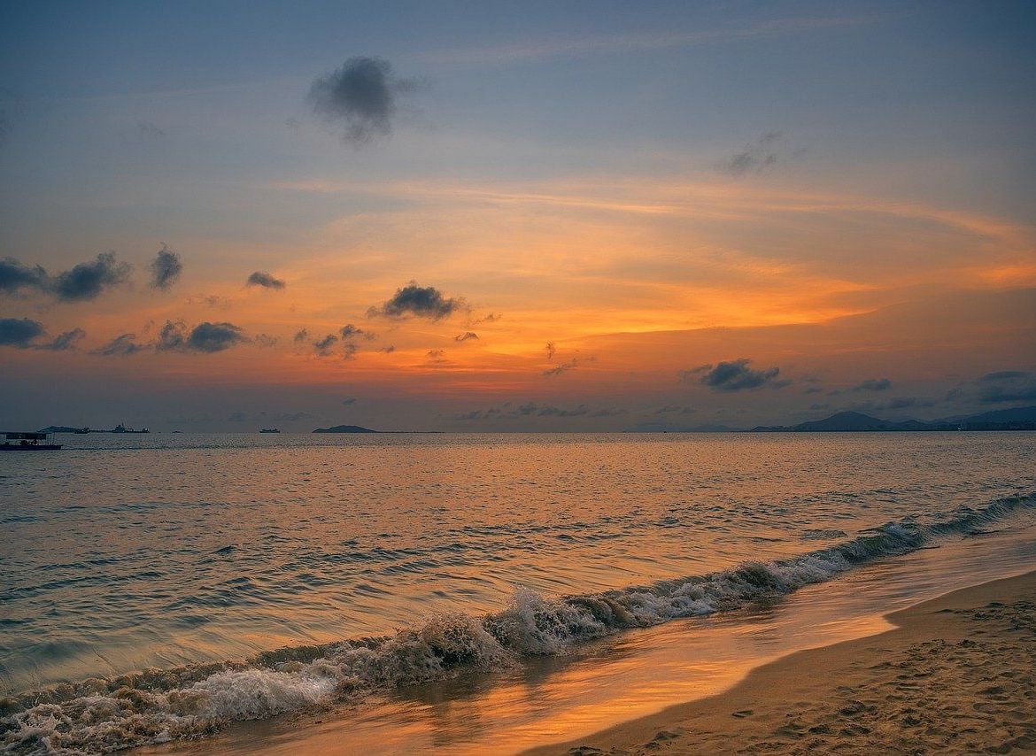 A serene beach view at sunset, with soft waves rolling onto the shore and the sky lit up in warm orange and purple hues.
