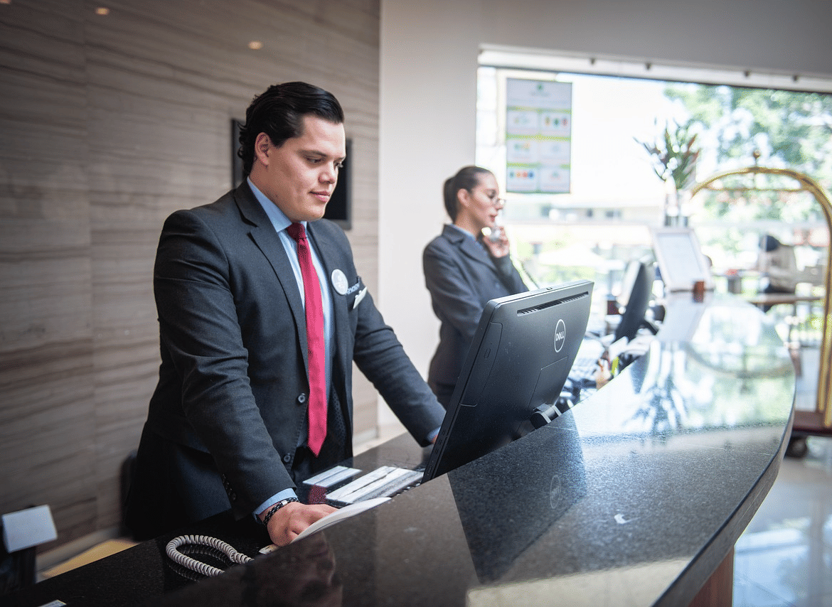 2 staff members standing behind the reception desk looking at the computer in front of them.