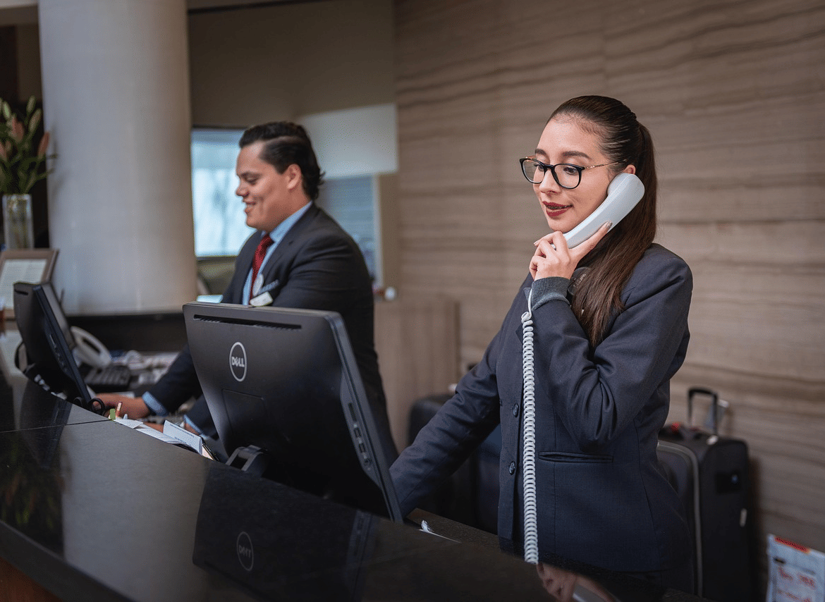A receptionist answering a landline phone at a hotel desk.