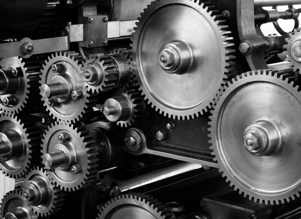 Close-up view of interconnected metal gears of various sizes in a mechanical system, showing detailed teeth and industrial machinery components.