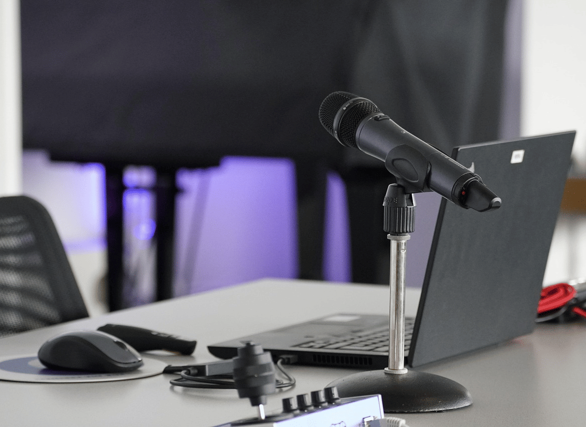 A desk setup featuring a microphone on a stand, a laptop, a computer mouse, and audio equipment in a workspace.