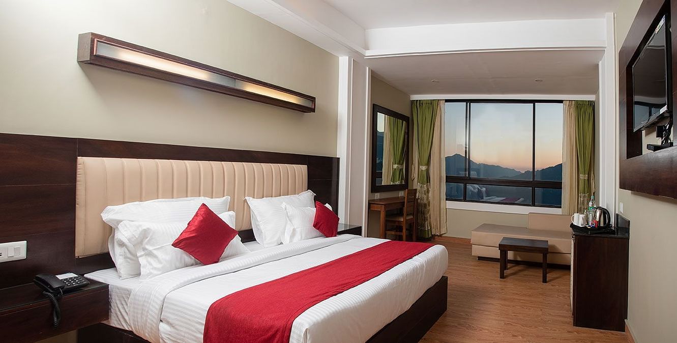 A room in Gangtok featuring a plush bed, bright lighting, a wall-mounted television, and a window with stunning views - Summit North Star, Gangtok