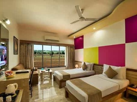 A modern room featuring twin beds with colourful wall panels and a television - Lion Lords Inn Rajula