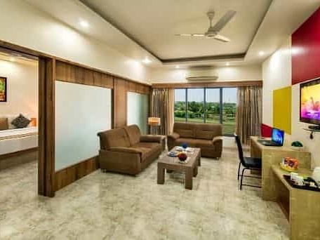 A spacious room including a seating area with sofas, a television, and large windows - Lion Lords Inn Rajula