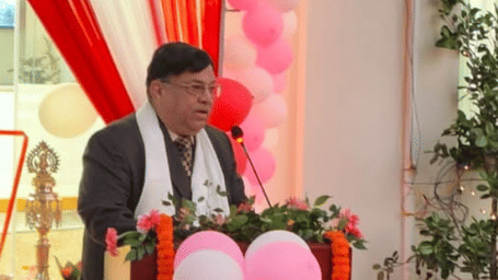  A man in a suit and white shawl speaks at a podium decorated with flowers and balloons.