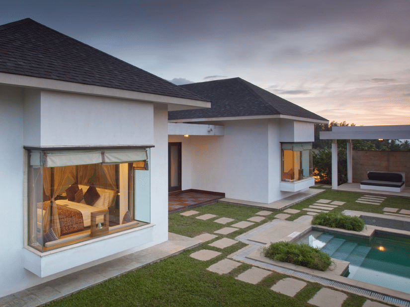 A modern resort villa at dusk with a private pool and a landscaped yard with stepping stones, located at The Serai Chikmagalur.